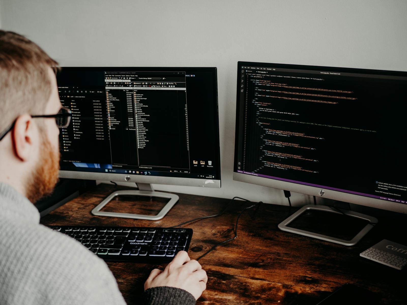 A programmer using dual monitors to code, featuring a keyboard and a wooden desk setup.