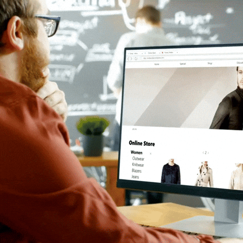 A man viewing an online clothing store on a computer screen, showcasing various apparel including outerwear and jeans.